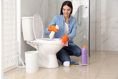 Young woman cleaning toilet bowl in bathroom