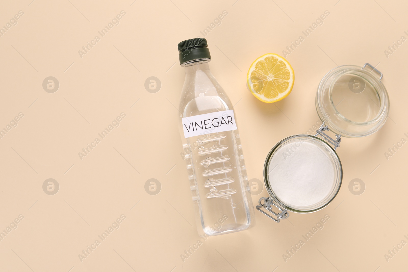 Photo of Eco friendly natural cleaners. Vinegar in bottle, cut lemon and jar of soda on beige background, flat lay. Space for text