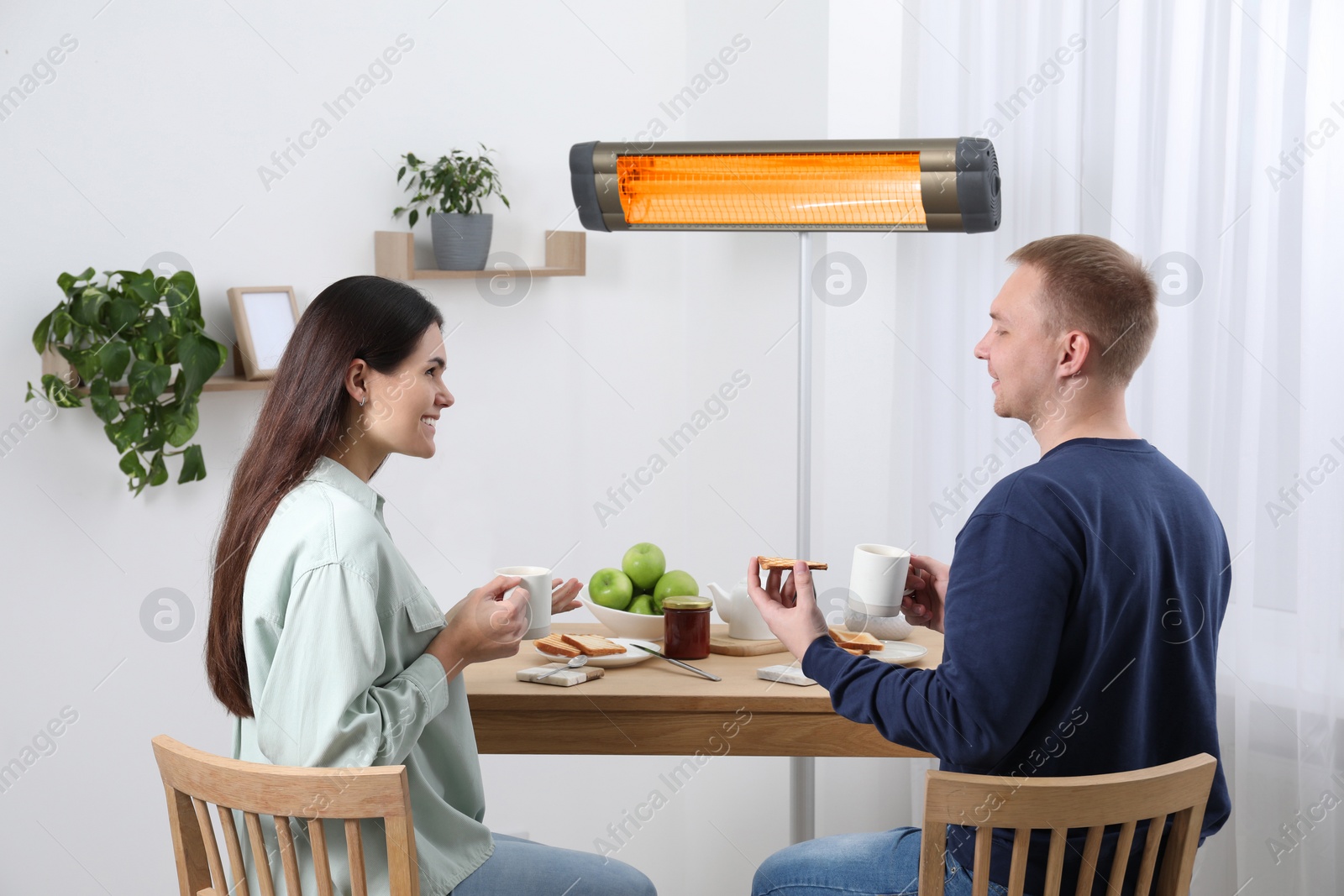 Photo of Couple spending time in room with modern electric infrared heater, focus on appliance