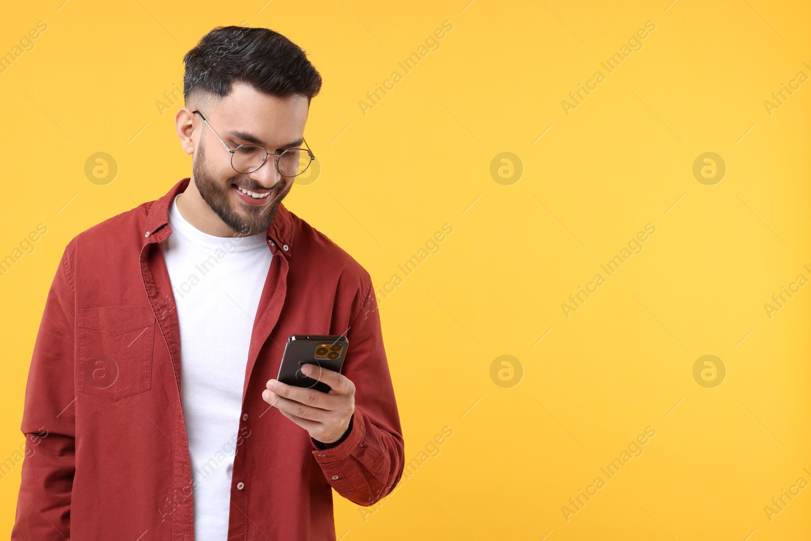 Photo of Happy young man using smartphone on yellow background, space for text