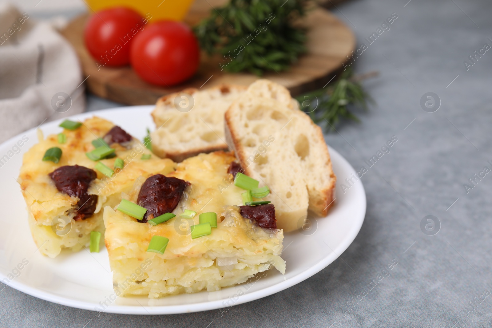 Photo of Tasty sausage casserole with green onion and bread on grey table, closeup