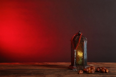 Photo of Muslim lamp, dates and prayer beads on wooden table against dark background. Space for text