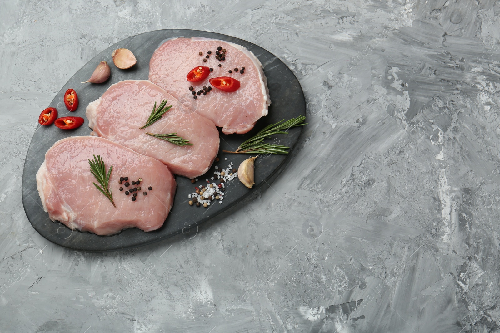 Photo of Pieces of raw pork meat, chili pepper and spices on grey textured table, top view. Space for text