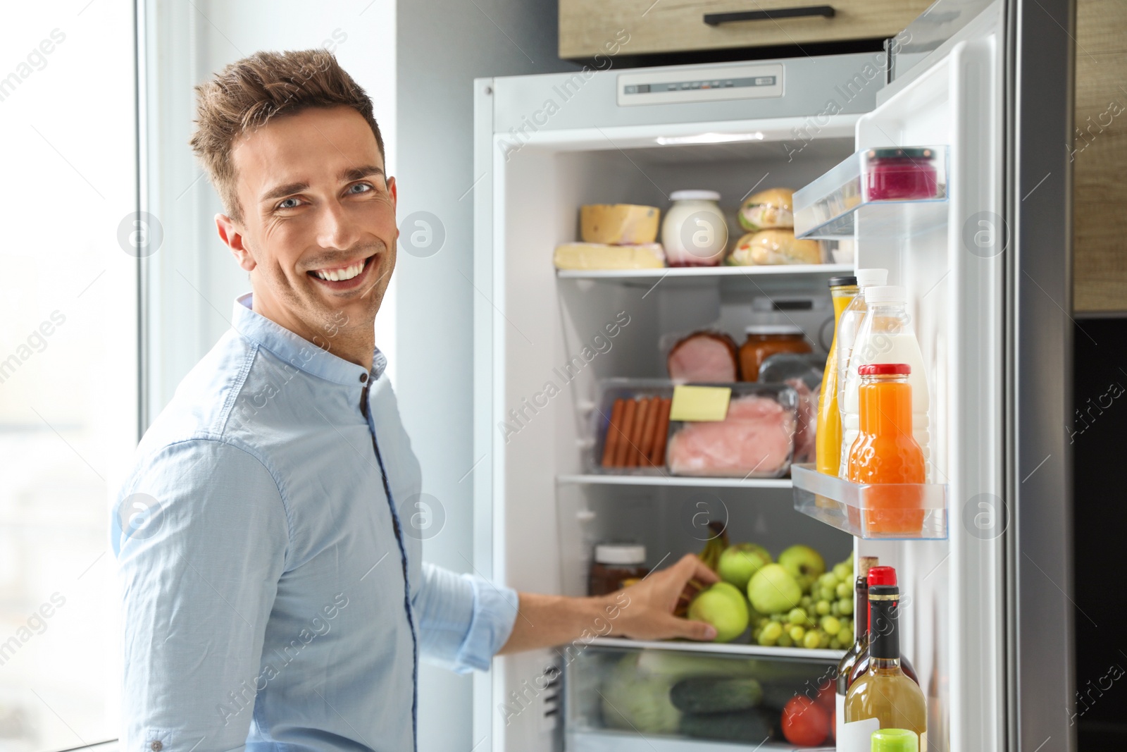 Photo of Man taking apple out of refrigerator in kitchen