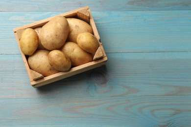 Raw fresh potatoes in crate on light blue wooden table, top view. Space for text