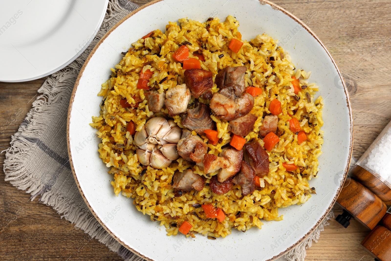 Photo of Delicious pilaf and salt on wooden table, flat lay