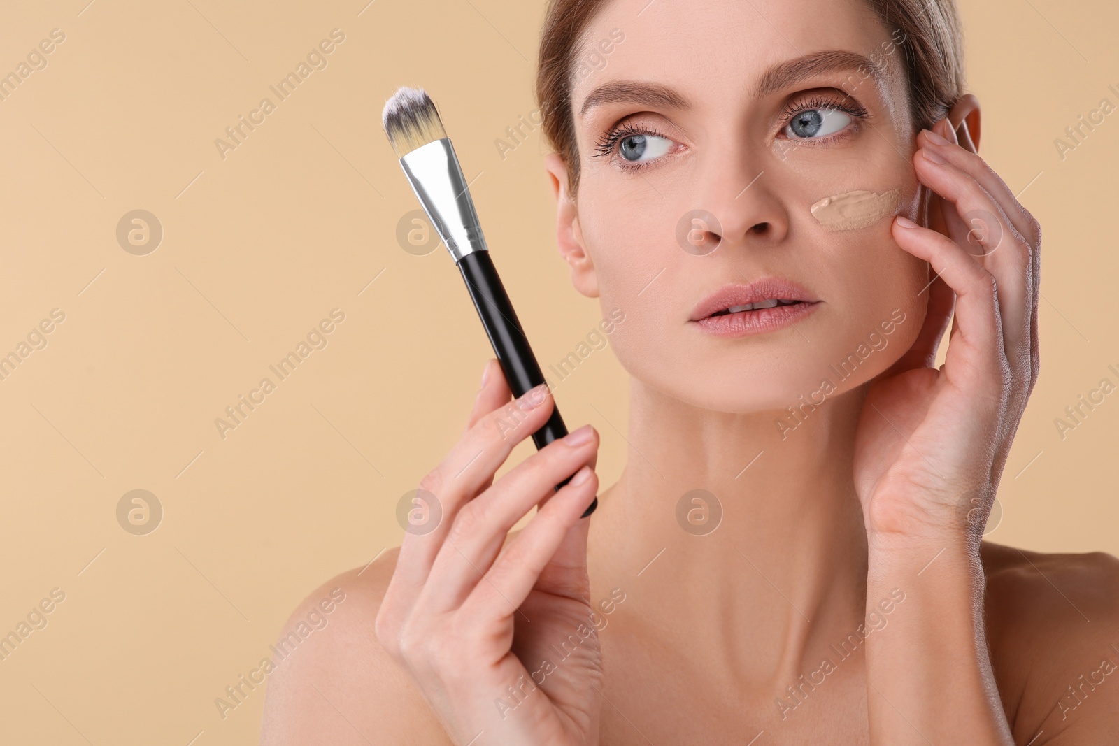 Photo of Woman with swatch of foundation holding makeup brush on beige background. Space for text