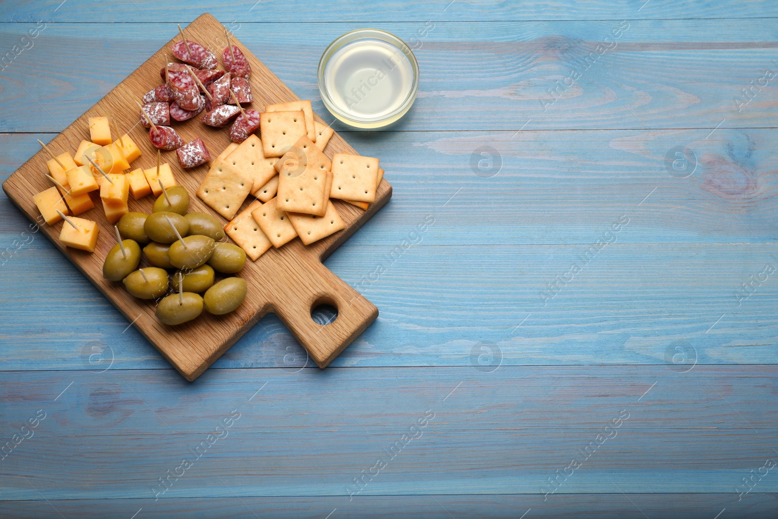 Photo of Toothpick appetizers. Pieces of cheese, sausage, olives and crackers on light blue wooden table, flat lay. Space for text