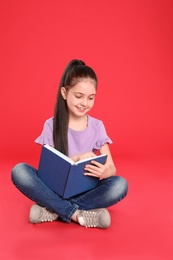 Cute little girl reading book on color background, space for text