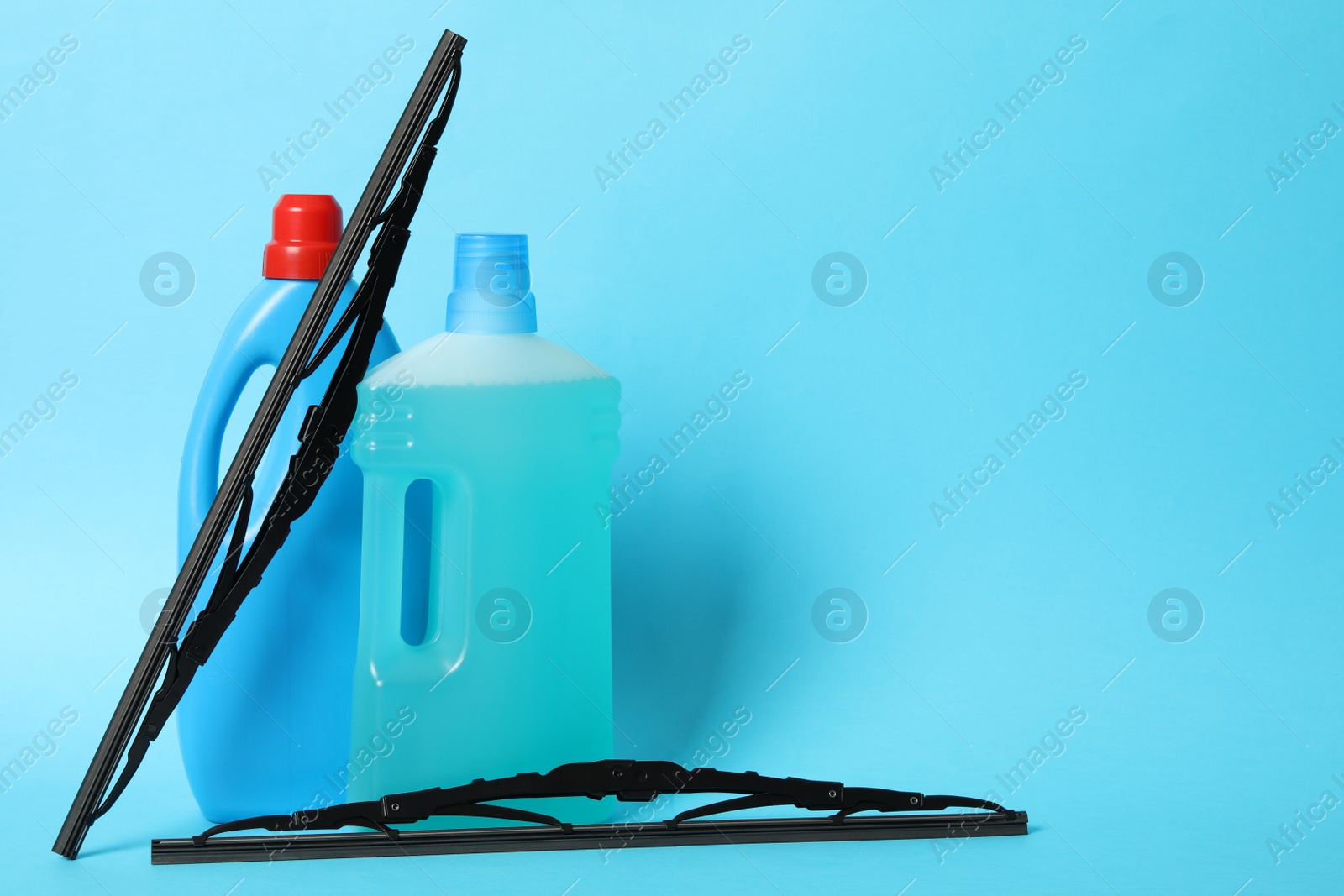 Photo of Bottles of windshield washer fluids and wipers on light blue background. Space for text