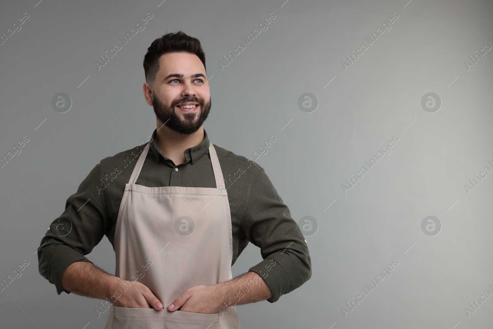 Photo of Smiling man in kitchen apron on grey background. Mockup for design