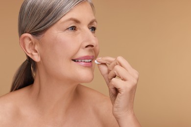 Beautiful woman taking vitamin pill on beige background, space for text