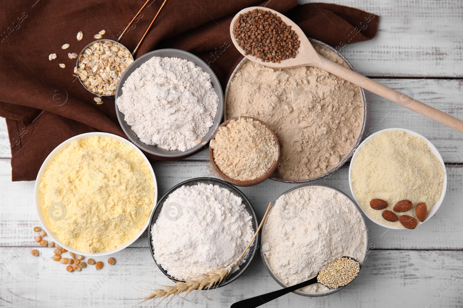 Photo of Bowls with different types of flour and ingredients on white wooden table, flat lay