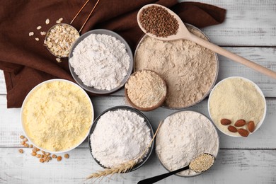 Bowls with different types of flour and ingredients on white wooden table, flat lay