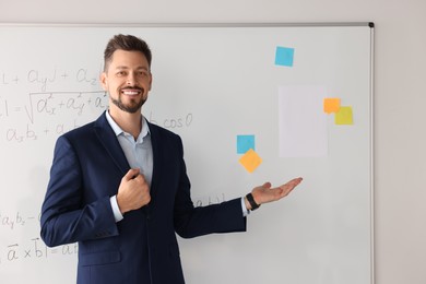 Photo of Happy teacher explaining mathematics at whiteboard in classroom