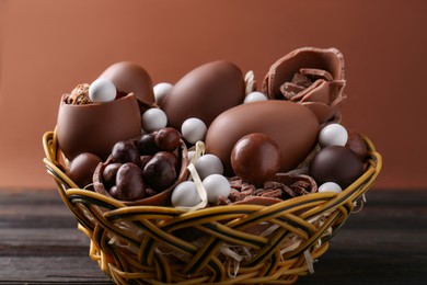 Tasty chocolate eggs and sweets in wicker basket on wooden table
