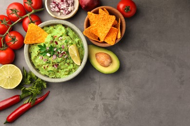 Photo of Bowl of delicious guacamole, nachos chips and ingredients on grey table, flat lay. Space for text