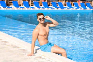 Handsome young man sitting at swimming pool edge on sunny day