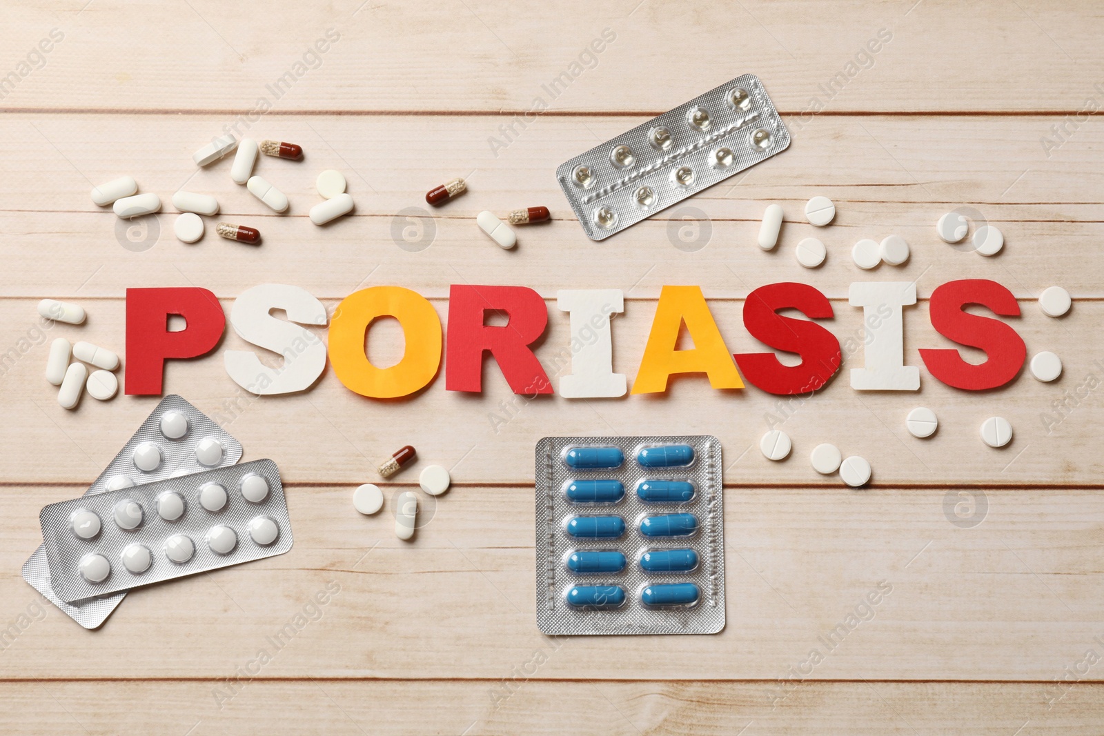 Photo of Word Psoriasis made of paper letters and pills on wooden table, flat lay