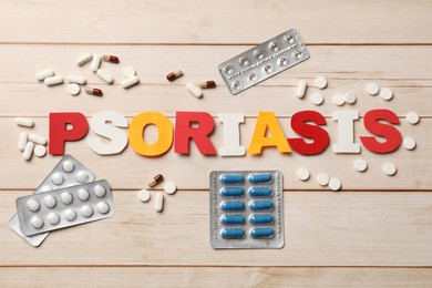 Word Psoriasis made of paper letters and pills on wooden table, flat lay