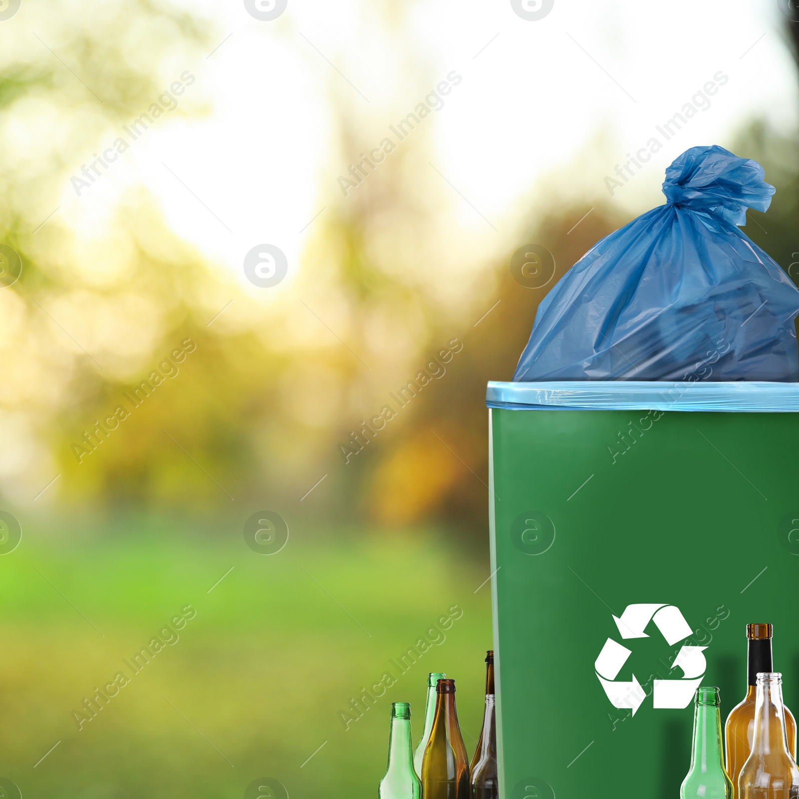 Image of Waste bin with plastic bag full of garbage and bottles on blurred background, space for text