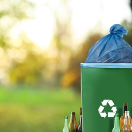 Waste bin with plastic bag full of garbage and bottles on blurred background, space for text