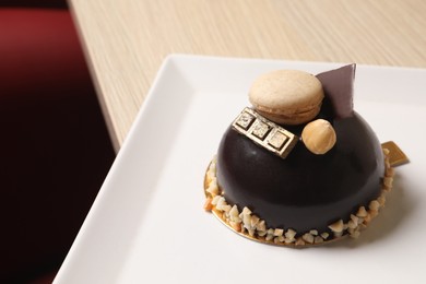 Photo of Delicious chocolate dessert decorated with nuts and macaron on table, closeup