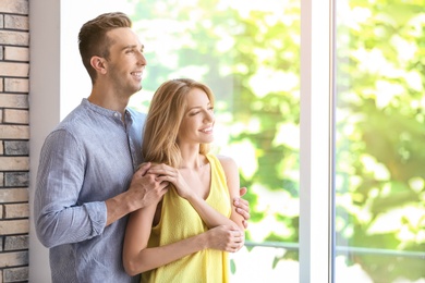 Happy young couple standing near window at home