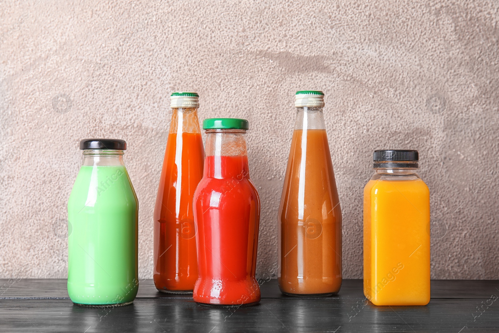 Photo of Bottles with different drinks on table against color background