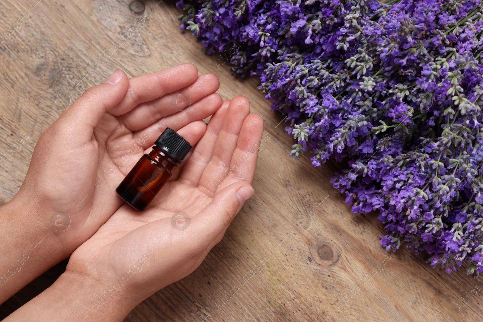 Photo of Woman with bottle of lavender essential oil and flowers on wooden background, top view