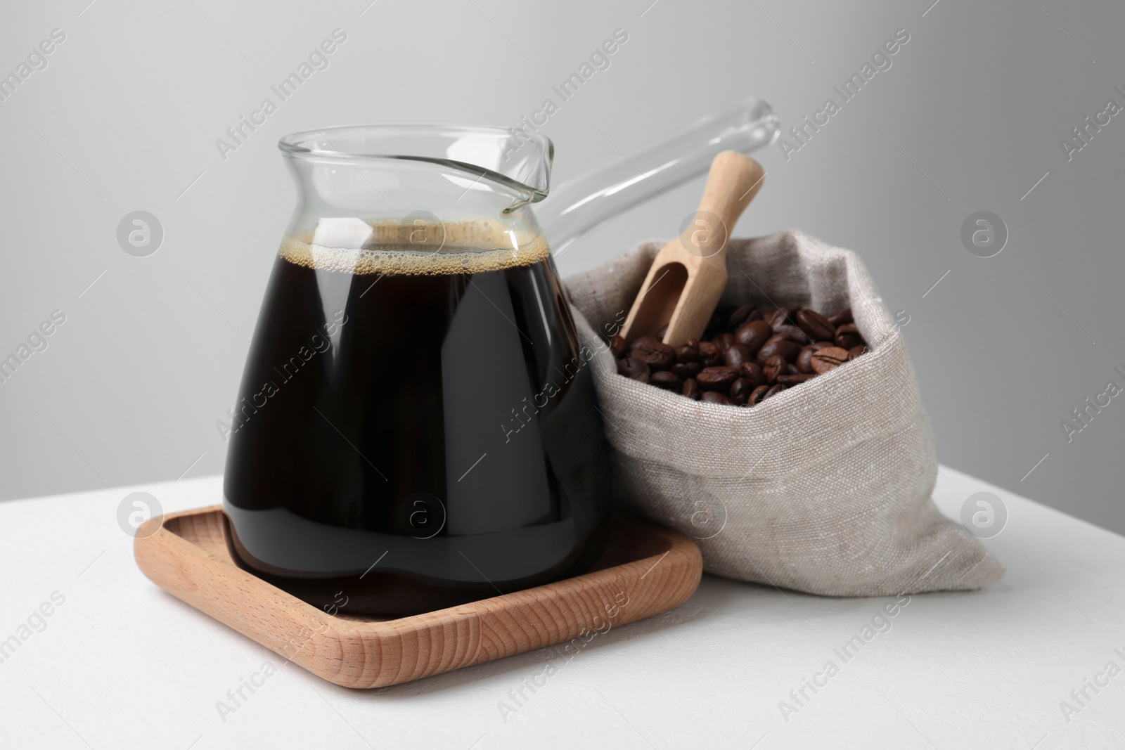 Photo of Turkish coffee in glass cezve and bag of beans on white table