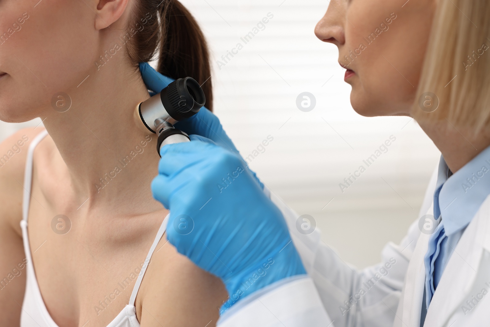 Photo of Dermatologist with dermatoscope examining patient in clinic, closeup