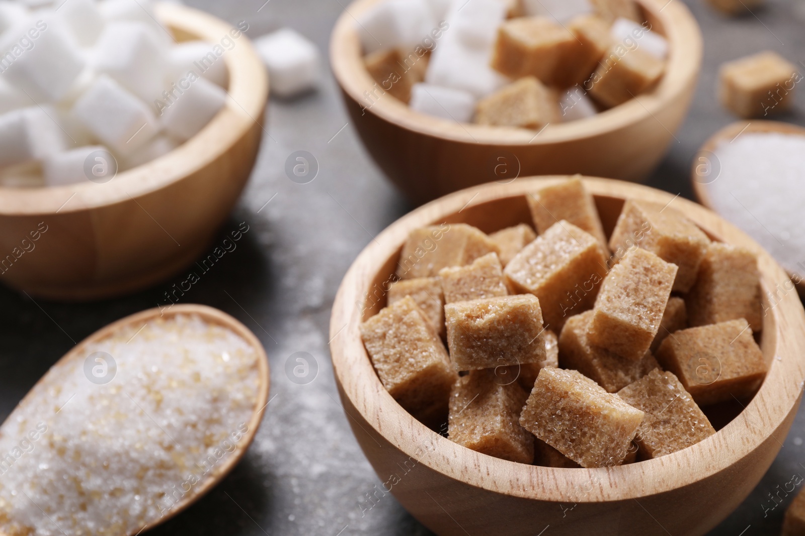 Photo of Bowls and spoon with different types of sugar on table, closeup