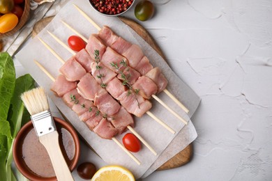 Photo of Flat lay composition of skewers with cut raw meat, thyme, tomatoes and marinade on light textured table. Space for text