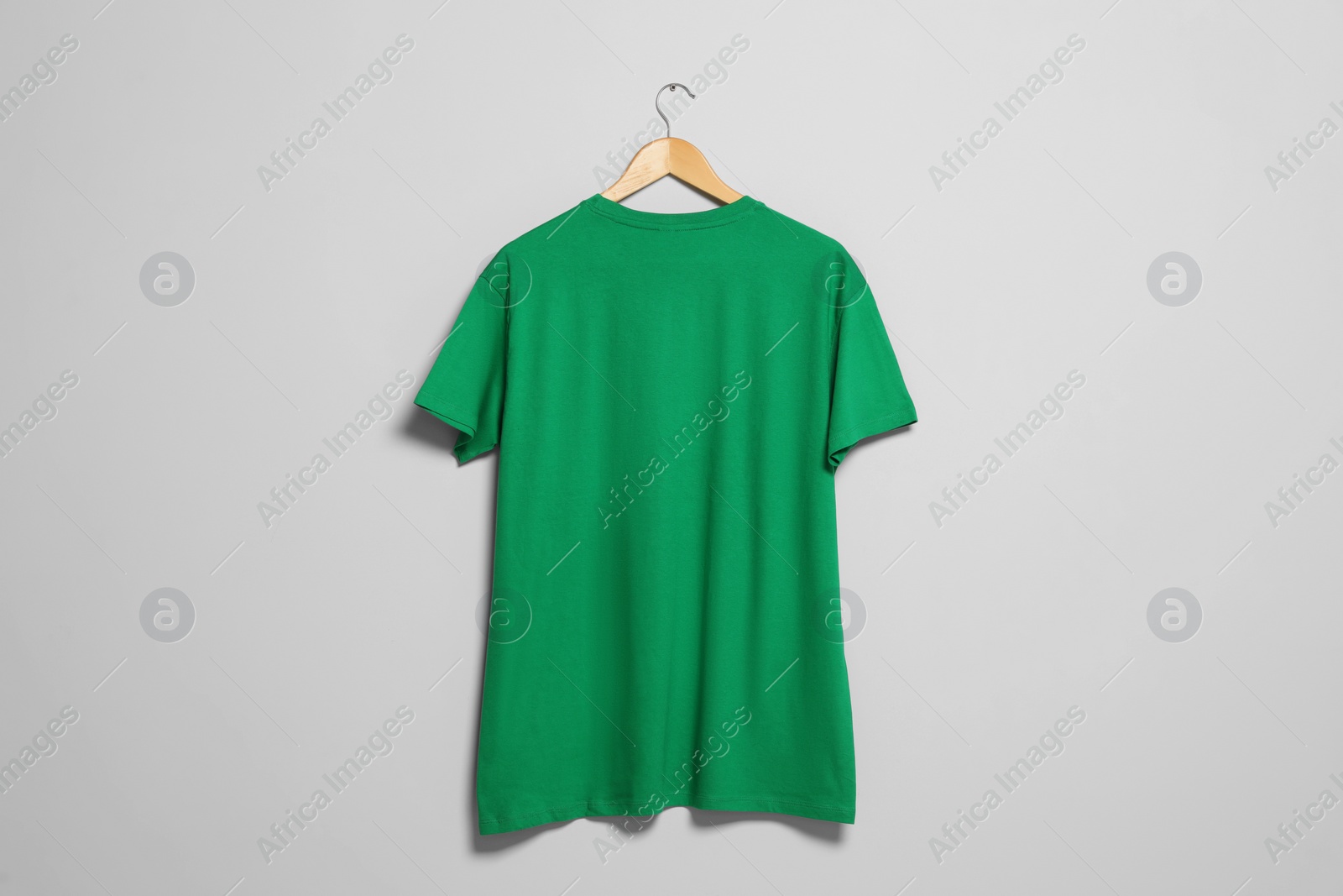 Photo of Hanger with green t-shirt on light wall. Mockup for design