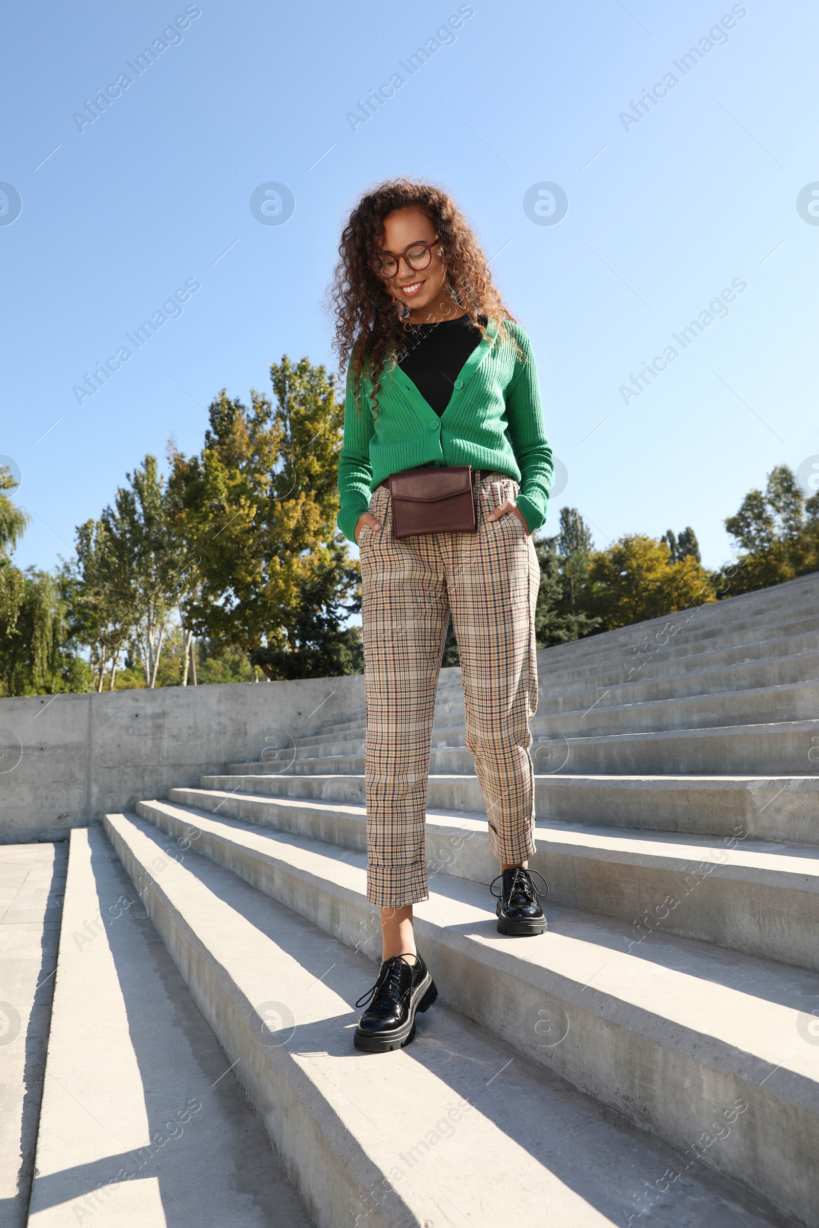 Photo of Beautiful African American woman with stylish waist bag on stairs outdoors