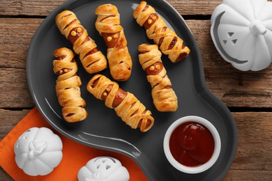 Cute sausage mummies served with ketchup on wooden table, flat lay. Halloween party food