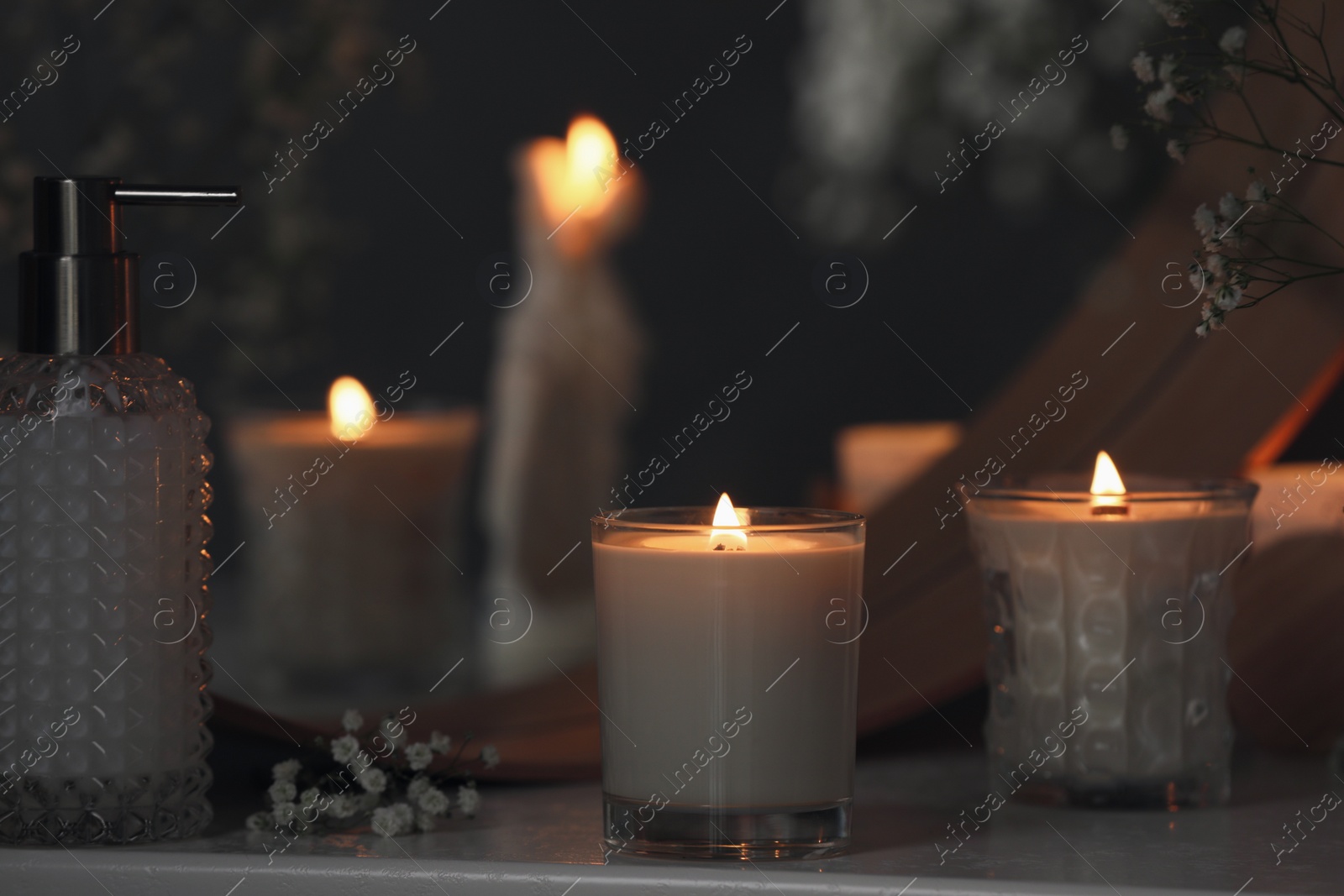 Photo of Beautiful burning candles and gypsophila flowers on white table near mirror indoors.