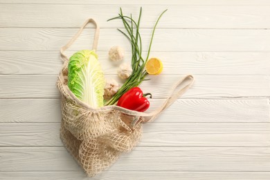 Photo of Fresh ripe Chinese cabbage and other vegetables in net bag on white wooden table, top view. Space for text