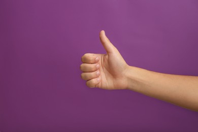 Photo of Teenage boy showing thumb up on purple background, closeup