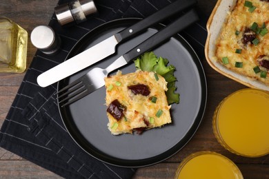 Photo of Tasty sausage casserole with green onions and cutlery served on wooden table, flat lay