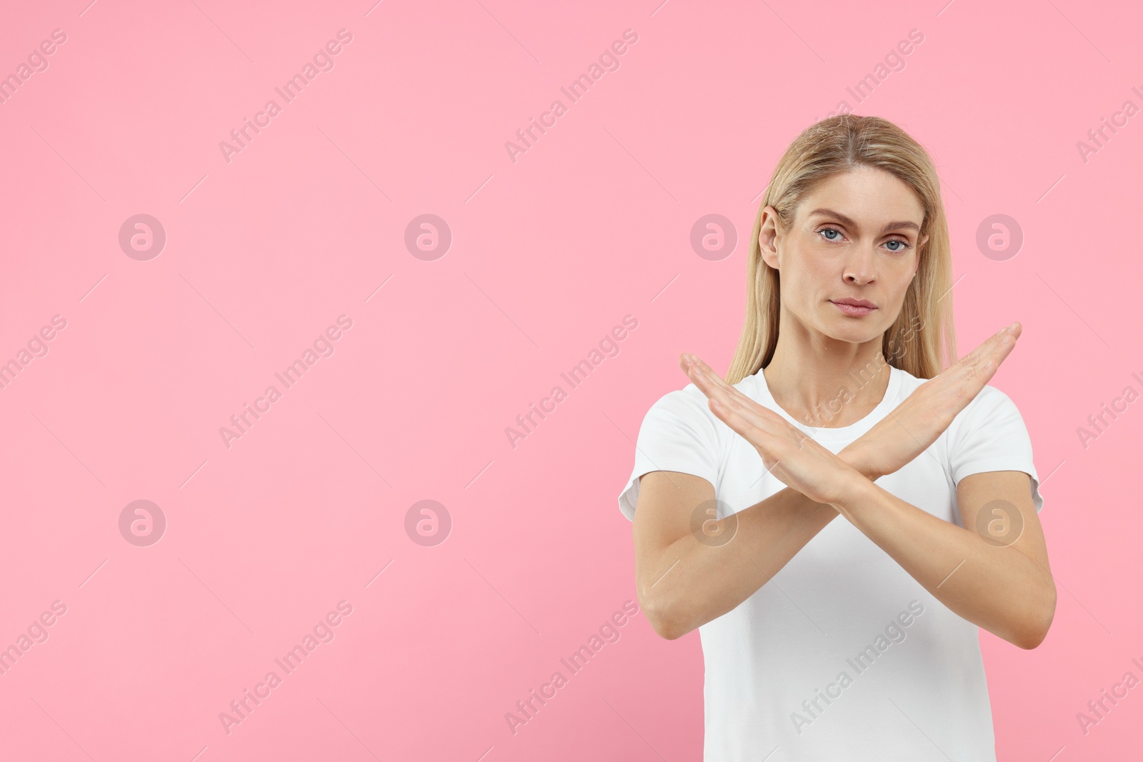 Photo of Stop gesture. Woman with crossed hands on pink background, space for text