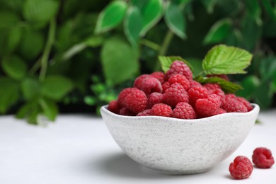 Photo of Bowl of fresh ripe raspberries with green leaves on white table against blurred background. Space for text