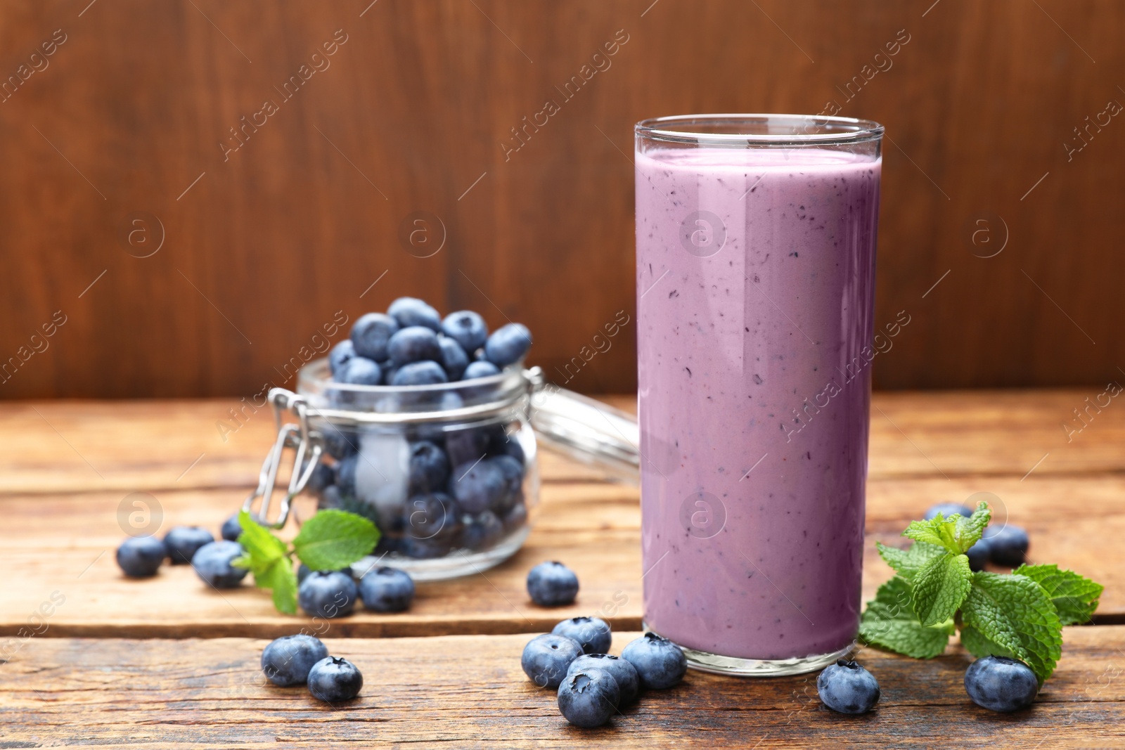 Photo of Glass of blueberry smoothie with mint and fresh berries on wooden table. Space for text