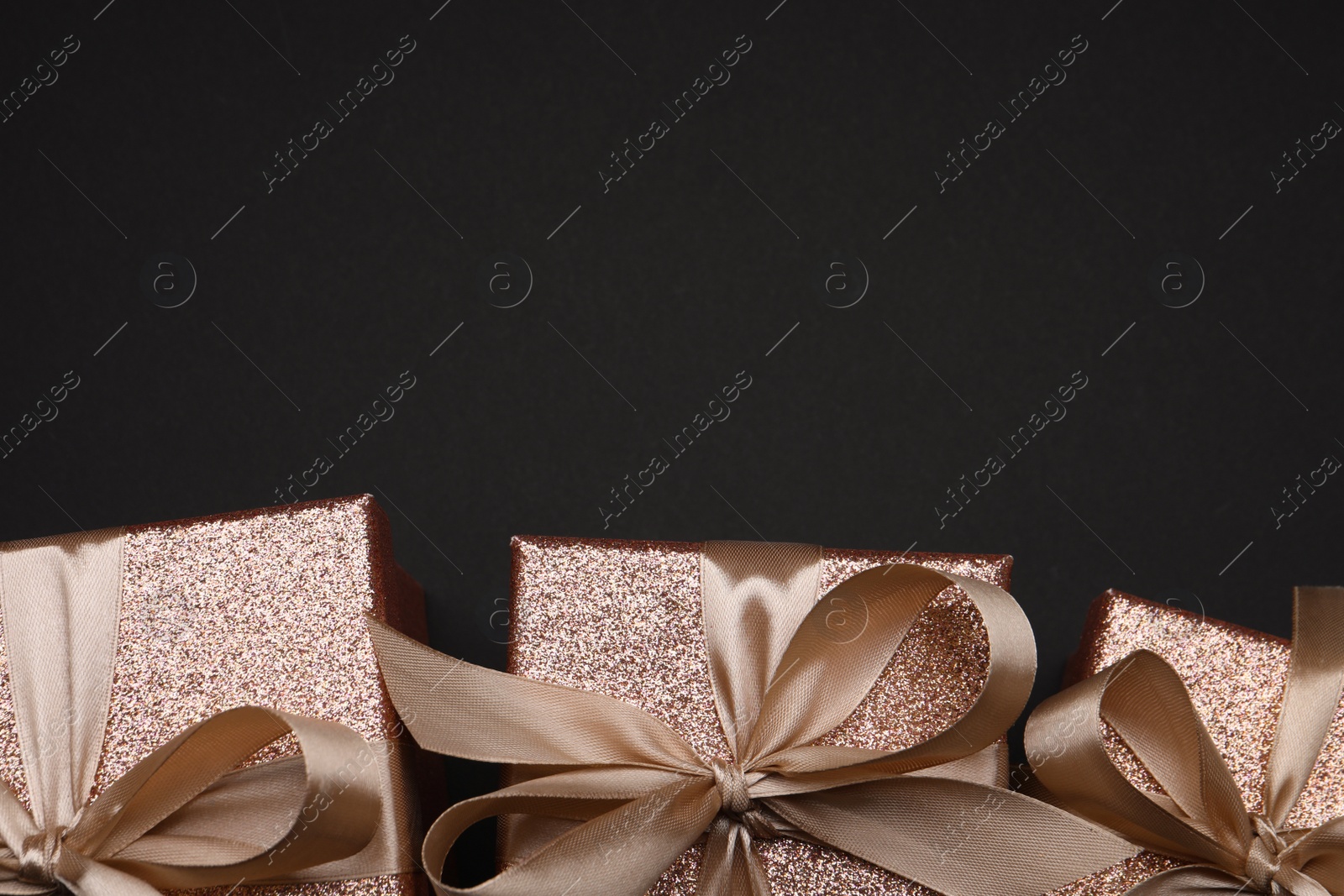 Photo of Shiny gift boxes with golden bows on black background, flat lay. Space for text