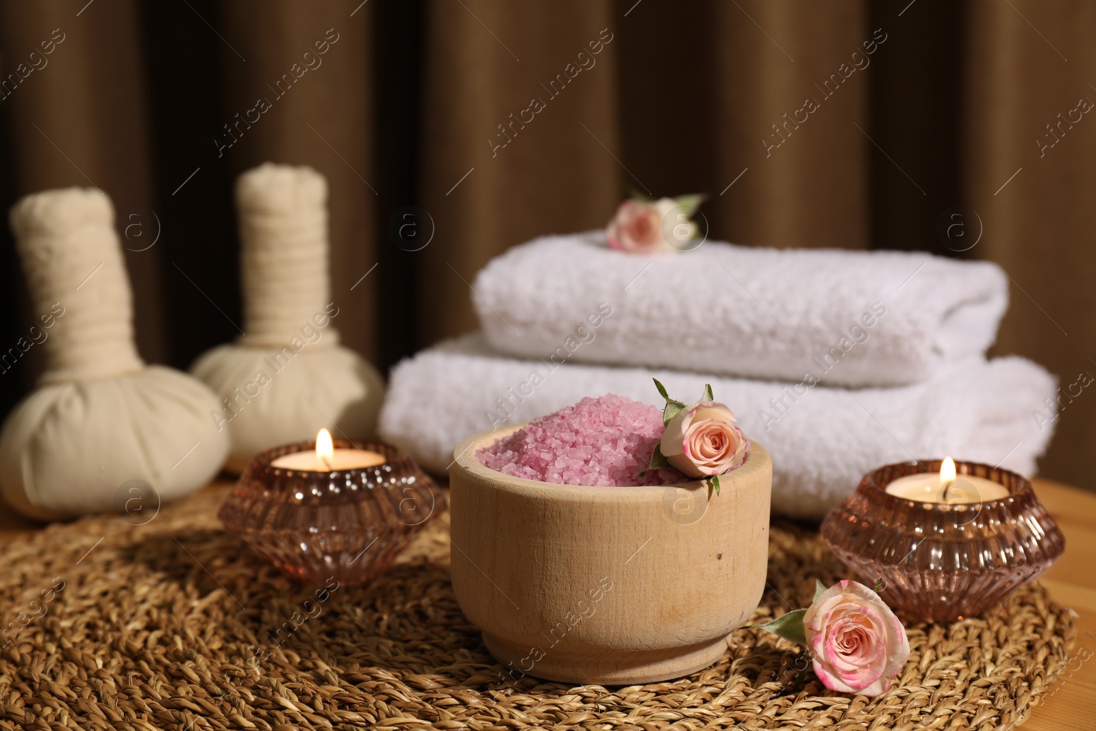 Photo of Bowl of pink sea salt, roses, burning candles and towels on wooden table