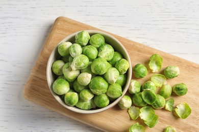 Board with bowl and Brussels sprouts on wooden background, top view