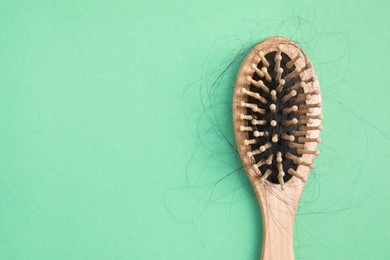 Photo of Wooden brush with lost hair on green background, top view. Space for text