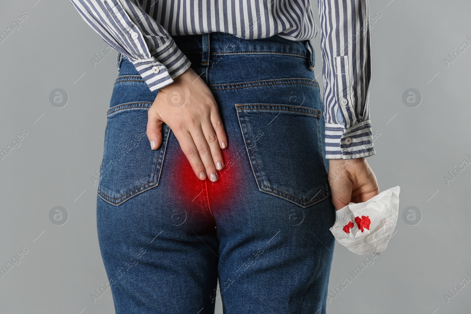 Image of Woman suffering from hemorrhoid and holding toilet paper with blood stain on grey background, closeup