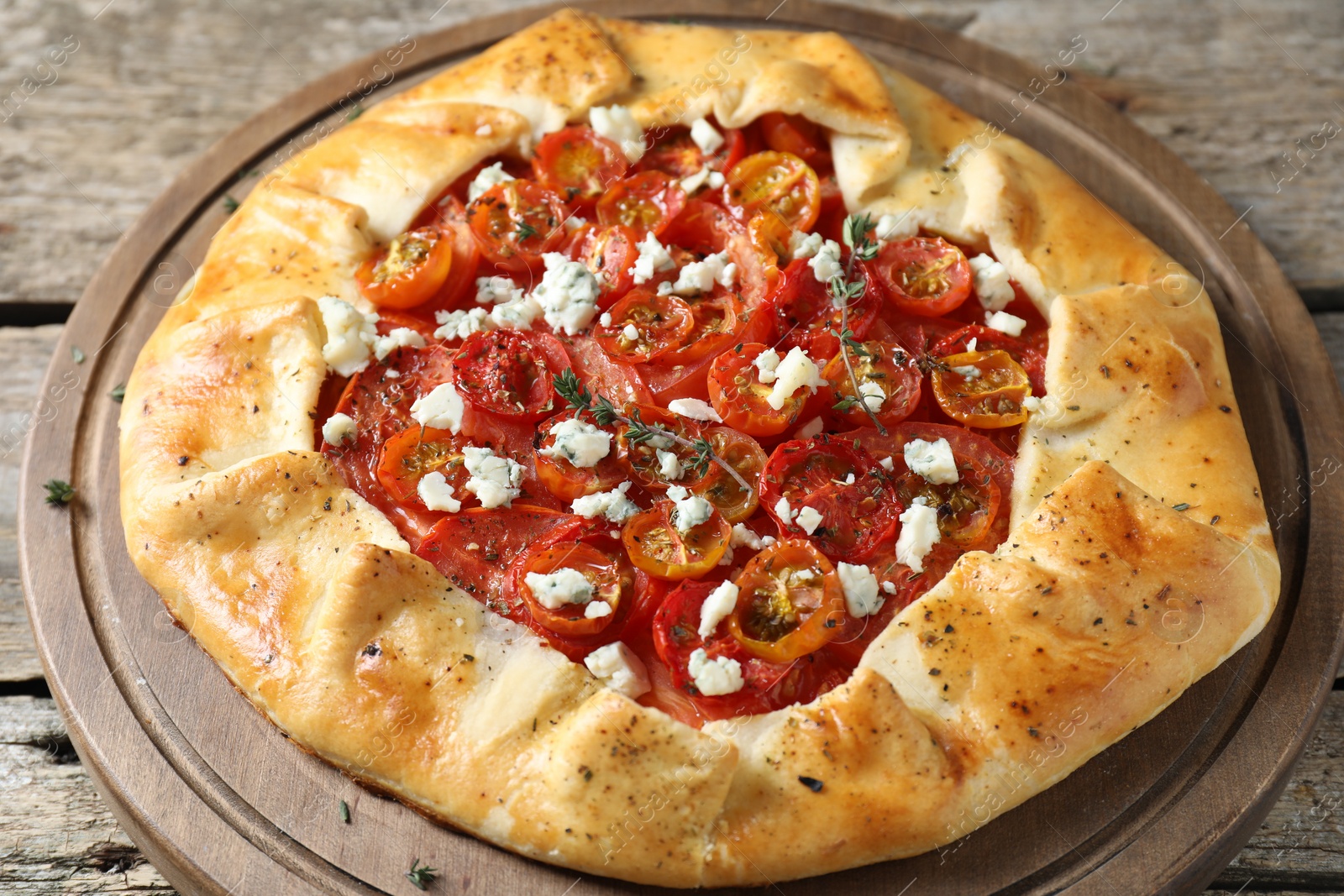 Photo of Tasty galette with tomato, thyme and cheese (Caprese galette) on wooden table, closeup